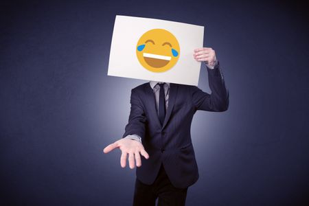 Young businessman hiding behind a laughing emoticon on cardboard