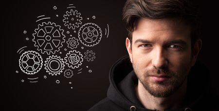 Portrait of a young businessman with rotating gears next to him on a dark background