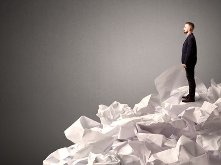 Thoughtful young businessman standing on a pile of crumpled paper with a deep grey background