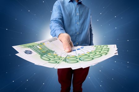 Young businessman holding large amount of bills with light beams behind him