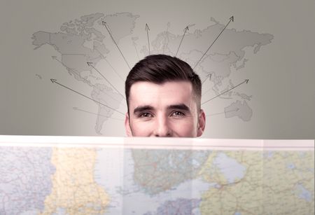 Handsome young man holding a map with world map and arrows behind him