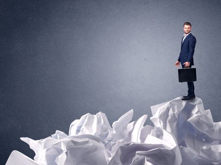Thoughtful young businessman standing on a pile of crumpled paper 