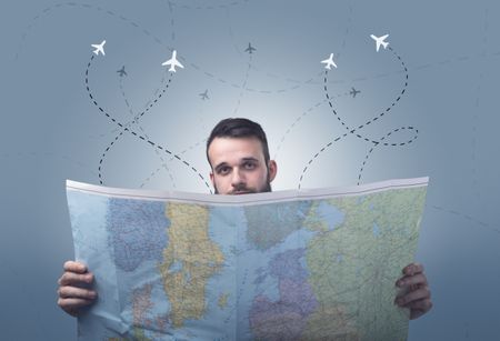 Handsome young man holding a map with little planes and their paths above him 