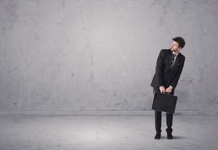A surprised young sales person in elegant suit standing in empty urban environment with grey concrete wall background concept