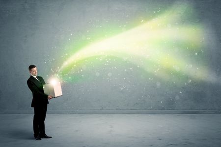 Bright yellow, green light beams escaping a cardboard box held by young elegant male business person in stylish suit concept.