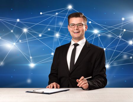 Young handsome businessman sitting at a desk with a blue connection graphic behnid him 