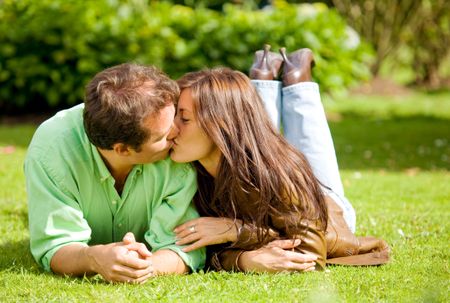 couple portrait kissing on the floor outdoors where both are looking happy