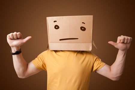 Young man standing and gesturing with a cardboard box on his head with straight face