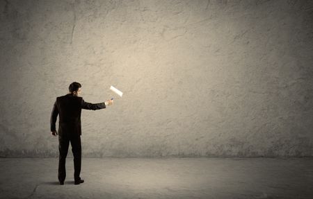 An elegant businessman in suit holding a paint roller, standing with his back, facing an empty urban concrete wall concept