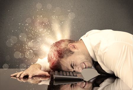 A young depressed business person laying his head on computer keyboard with thoughts exploding from his head illustrated by light beams concept
