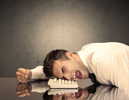 A sad and depressed office worker resting his head on a keyboard while shouting in front of a grey grungy wall background