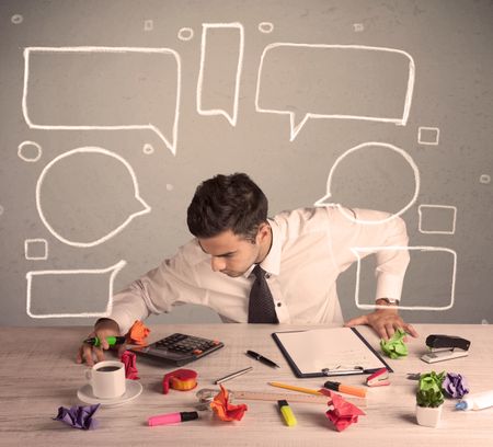 An intelligent elegant business person sitting at a desk and working with drawn empty text bubbles, boxes around him concept