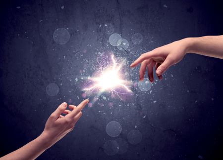 Two male hands reaching towards each other, almost touching with fingers, lighting spark in galaxy background concept
