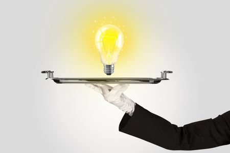 Serving a bright business idea concept using a bulb with bright sparkling warm yellow light presented on a silver plate
