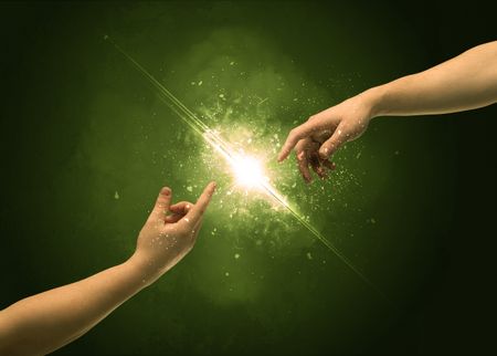 Two naked male hands about to touch, lighting the spark with modest explosion in front of green background concept