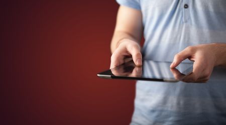 Close up of hand holding digital touchpad tablet device on background