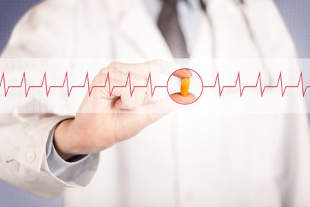male-doctor-white-coat-stethoscope-shoulder-593353058 A male doctor in white coat with a stethoscope on one shoulder holding a pill between his fingers focused on a heartbeat graph