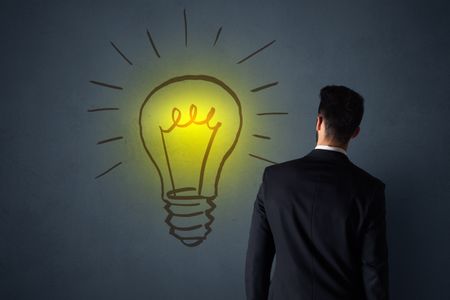 Young businessman in black suit standing in front of a drawn yellow lightbulb 