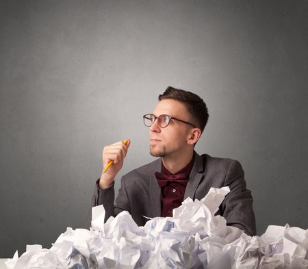 Young businessman sitting behind crumpled paper with grey background 