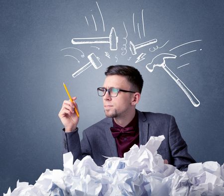 Young businessman sitting behind crumpled paper with drawn hammers hitting his head