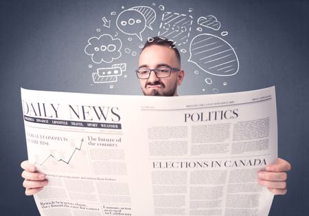 Puzzled young businessman reading daily newspaper with speech bubbles above his head