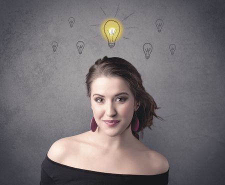 A teen student girl with funny facial expression has a good idea illustrated by a drawn light bulb lighting up above the head on the grey wall background concept.