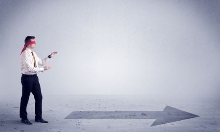 A confused blind salesman standing in front of a drawn arrow on the floor pointing in the right direction concept.