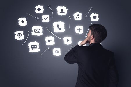 Young businessman in black suit standing in front of white multimedia icons