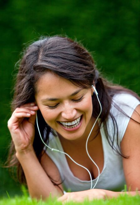 Happy woman lying on grass listening to music outdoors