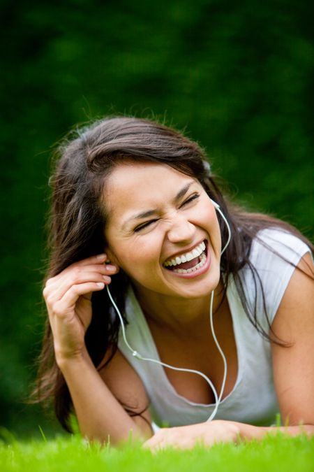 Happy woman lying on grass listening to music outdoors and laughing