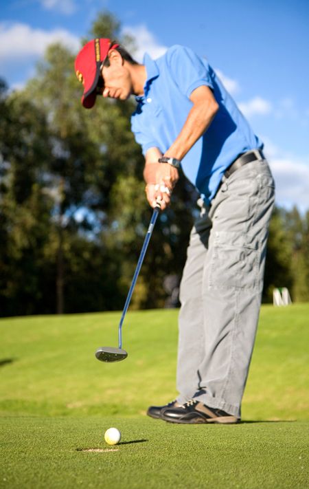 male golfer in putting green about to put the ball in the hole
