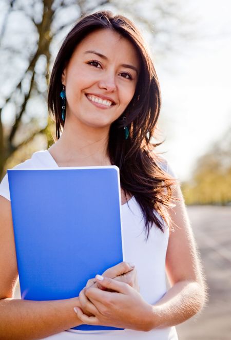 Female student outdoors holding a notebook and smiling