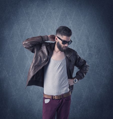 A handsome fashion model with beard standing in front of fancy background and making funny faces while using a vintage camera concept