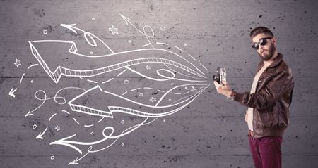A hipster guy opening his point of view through looking a vintage camera concept with illustratied drawn arrows on urban wall