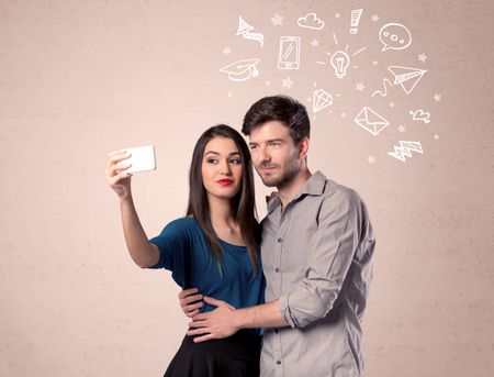 A young couple in love taking selfie with a mobile phone in the handsome guy's hand and drawn media communication icons above them, confused ideas concept