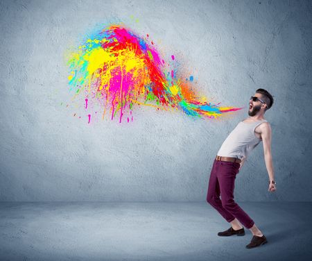 A funny hipster person in casual urban clothing shouting bright colorful paint on city wall concept