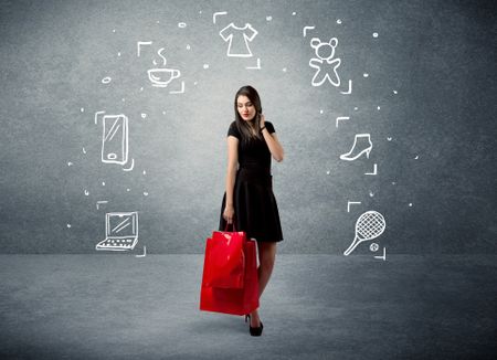 A beautiful young girl in black standing with red shopping bags in front of urban wall background and laptop, shoes, tennis icons concept