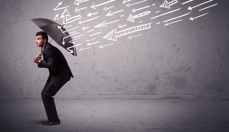 Business man standing with umbrella and drawn arrows hitting him on grungy background