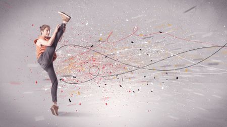 A young contemporary energetic dancer in action in front of a grey wall background with lines, spray dots and splatter concept