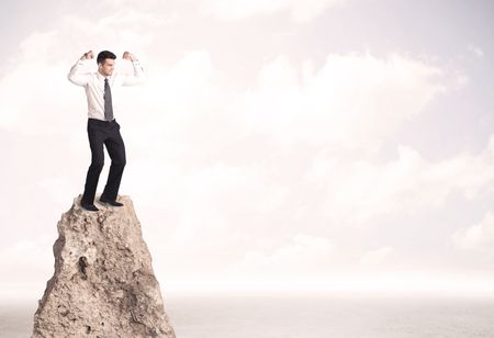 Successful sales person with brief case standing on top of a mountain cliff edge looking above the landscape between the clouds