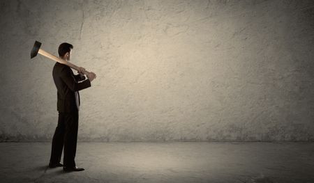 Business man standing in front of a grungy copyspace wall with a hammer