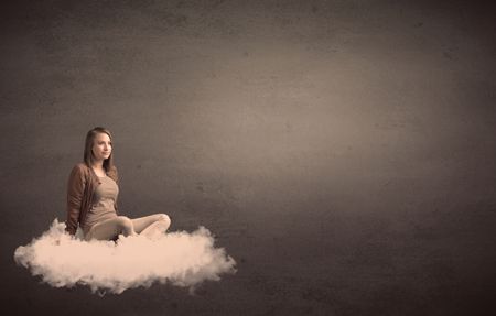 Caucasian woman sitting on a white fluffy cloud daydreaming beside a plain grunge background