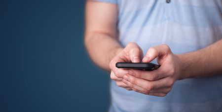 Young man holding smarthphone in hand while typing