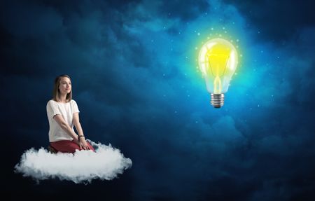 Caucasian woman sitting on a white fluffy cloud looking and wondering at a big, bright, shiny, glowing yellow lightbulb