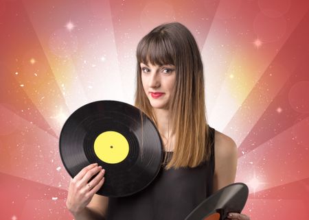 Young lady holding vinyl record on a red background with lights shining behind her