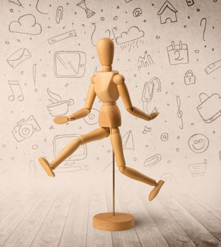 Wooden mannequin posed in front of a greyish background with mixed media scribbles behind it