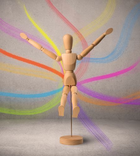 Wooden mannequin posed in front of a greyish background with colorful lines behind it