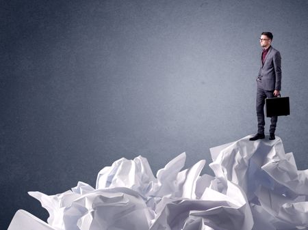 Thoughtful young businessman standing on a pile of crumpled paper 