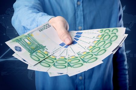 Young businessman holding large amount of bills with blue charts in the background