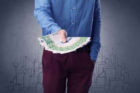 Young businessman holding large amount of bills with grungy drawings of a city and numbers behind him